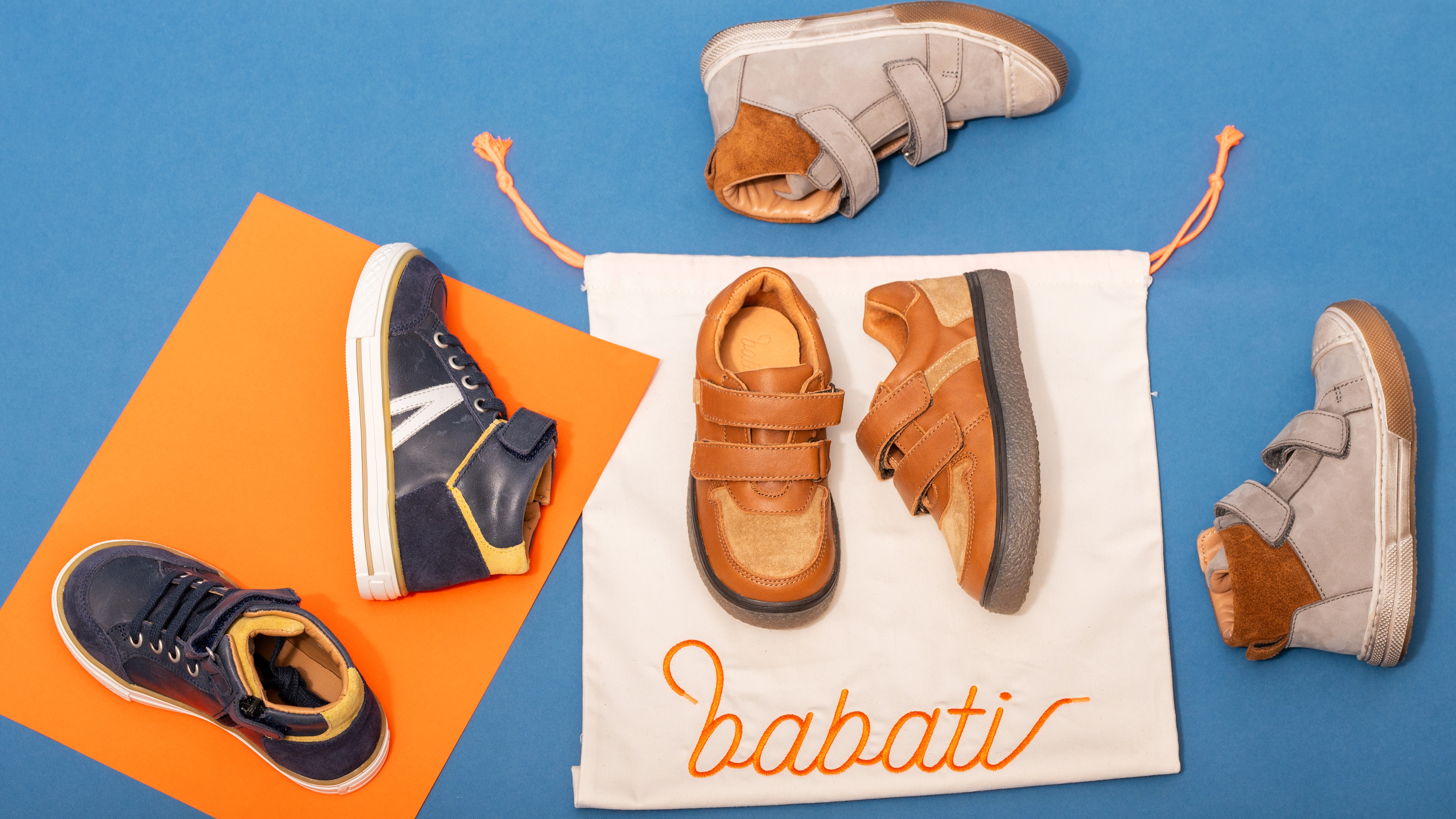 Chaussures pour enfants Babati en flat lay sur fond bleu et orange