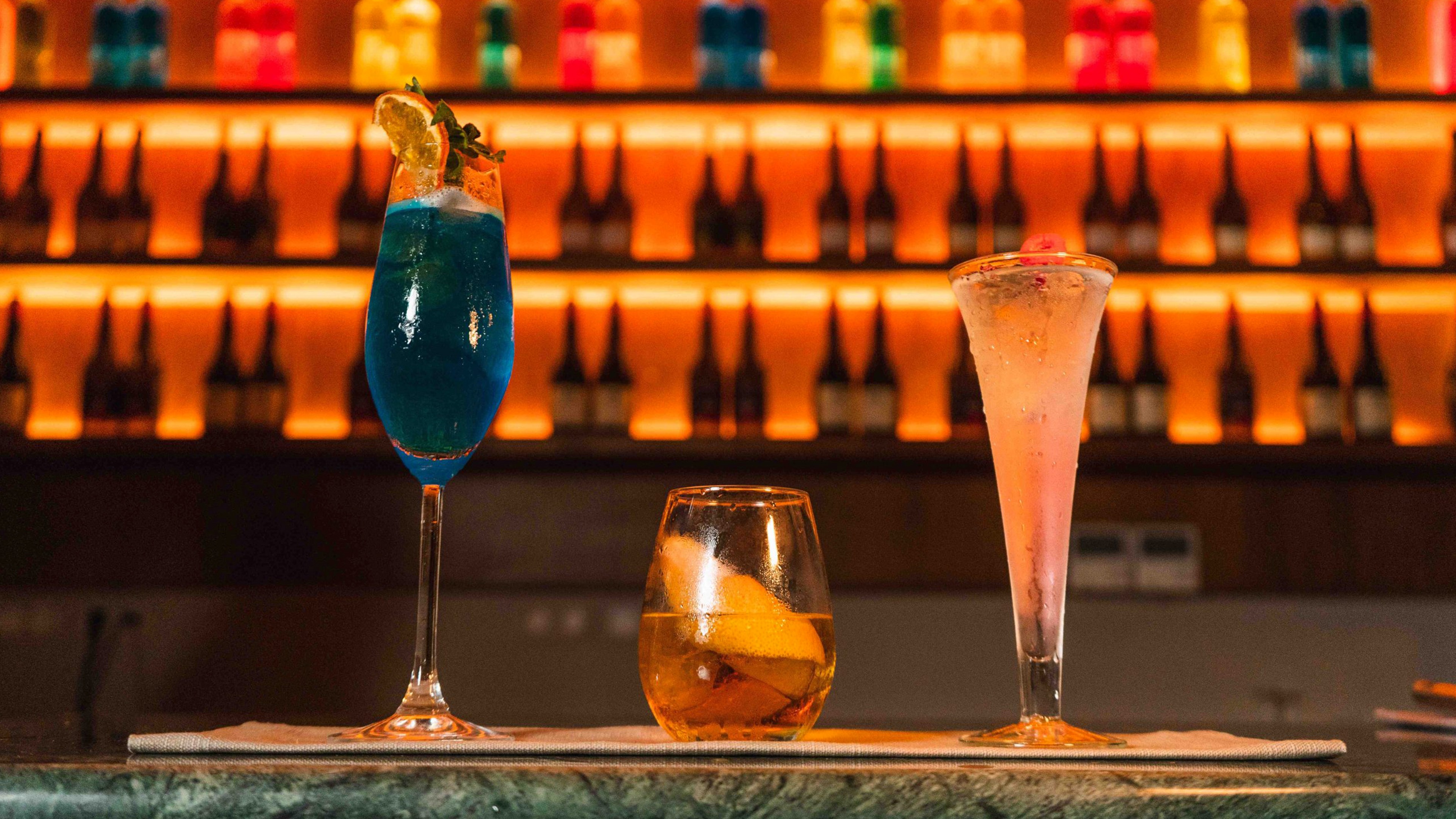 Trois cocktails colorés sur un comptoir de bar éclairé en orange