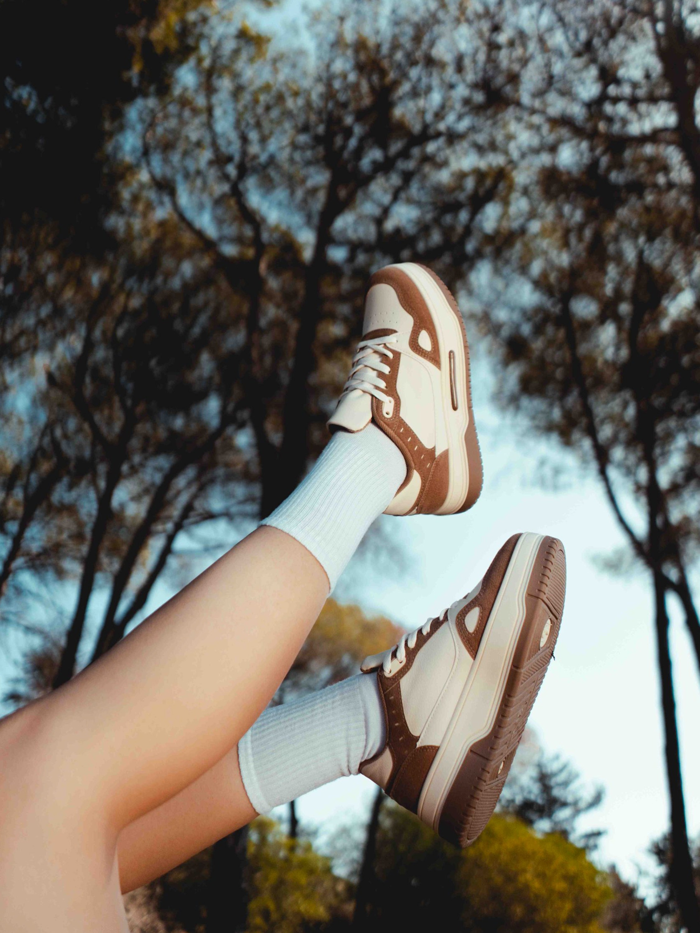 Jambes levées portant des baskets blanches et marron sous les arbres