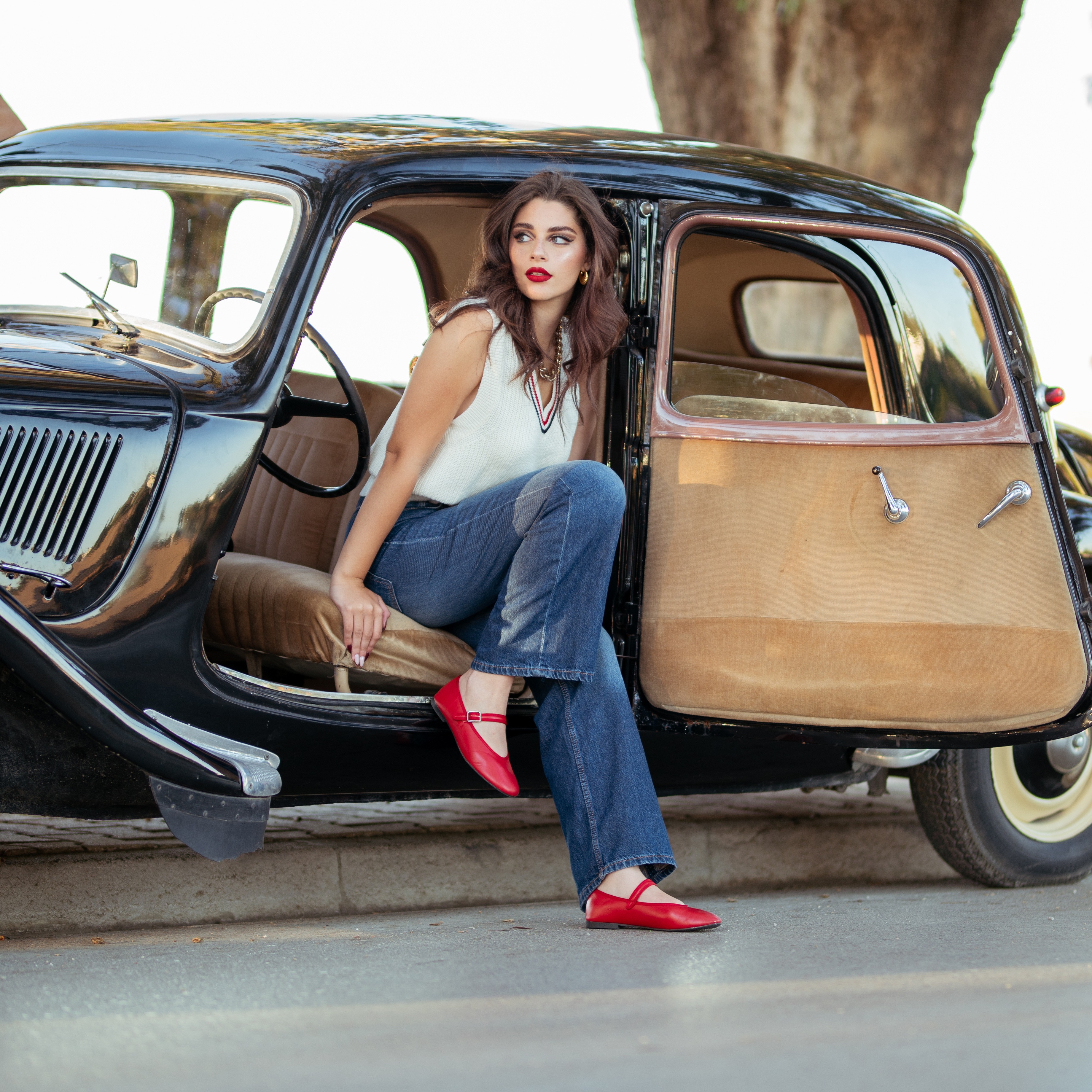 Femme en ballerines rouges assise dans une voiture ancienne noire