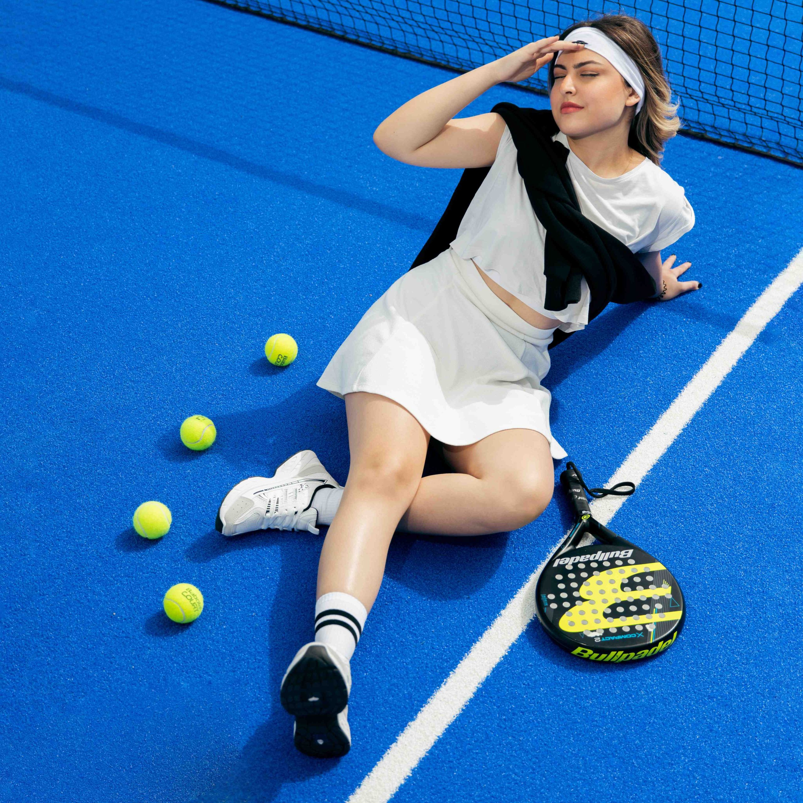 Shooting tenue de sport padel : femme en blanc sur un terrain bleu avec raquette Bullpadel